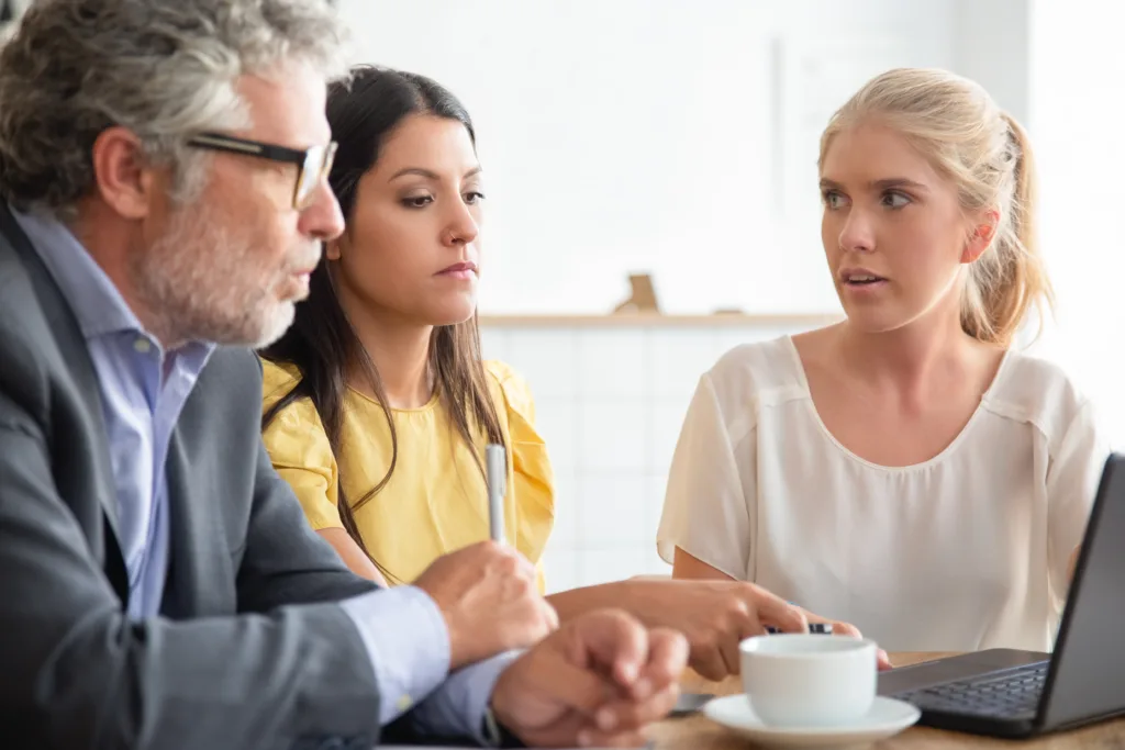 Father discussing estate planning with his two daughters while reviewing important documents on a computer at home.